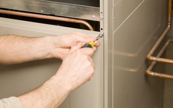 Removing a furnace access panel with a screwdriver to diagnose it