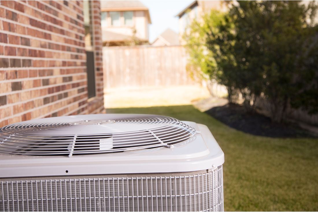 Residential air conditioning condenser beside a brick home